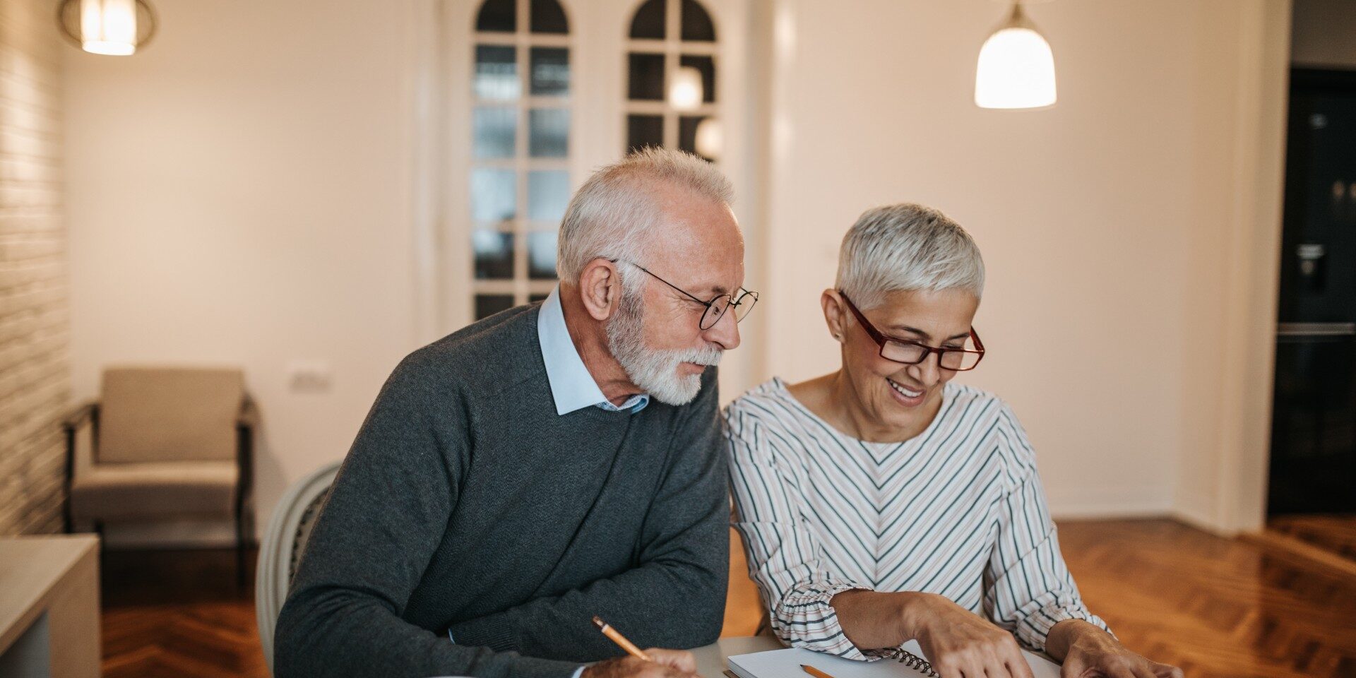 We might just be able to afford that vacation! A happy senior couple calculating their finances in a beautiful home.